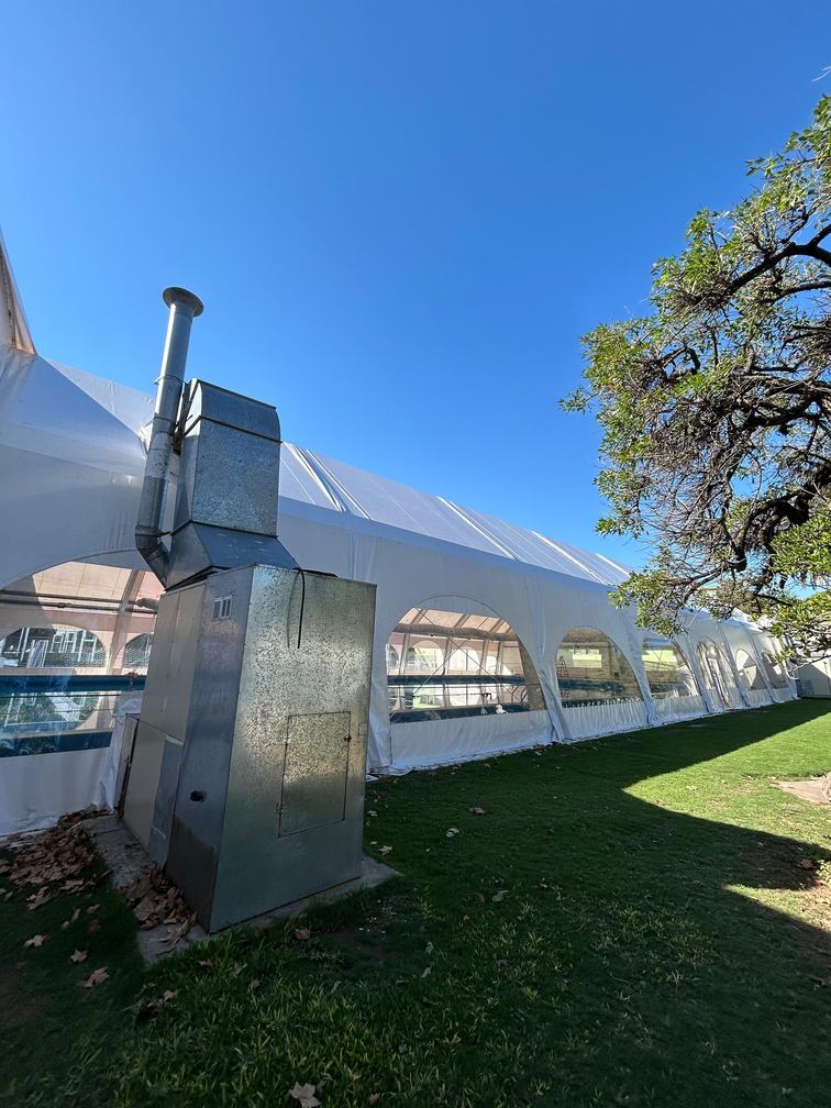 Equipo de climatización exterior conectado a la carpa mediante un conducto metálico