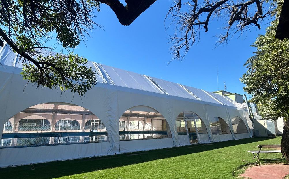 Carpa de lona blanca de grandes dimensiones que cubre una pileta de natación olímpica